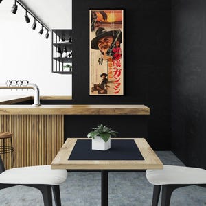 a modern, minimalist interior design with a black and white color scheme. A large poster of a man is prominently displayed on the wall, adding a unique visual element to the space. In the foreground, there is a wooden table with two white chairs, creating a cozy seating area. The overall design has a sleek and contemporary feel, with the black and white color palette contributing to the overall aesthetic.