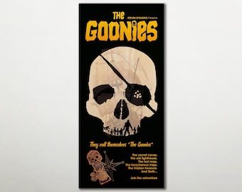 Könnte beinhalten: Ein rechteckiges Poster mit einem großen beigen Totenkopf mit Augenklappe auf schwarzem Hintergrund. Der Text lautet THE GOONIES, STEVEN SPIELBERG Presents, They call themselves The Goonies und The secret caves. The old lighthouse. The lost map.