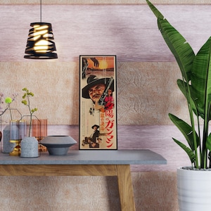 a modern interior design with a wooden table, a potted plant, and various decorative items such as vases and a bowl. There is a framed poster on the wall with Japanese text, and a hanging light fixture above the table.