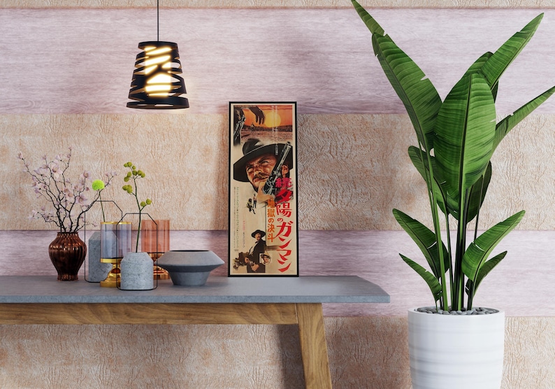 a modern interior design with a wooden table, a potted plant, and various decorative items such as vases and a bowl. There is a framed poster on the wall with Japanese text, and a hanging light fixture above the table.