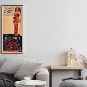a framed vintage poster of a woman in a red dress, hanging on a wall above a gray couch in a living room setting.