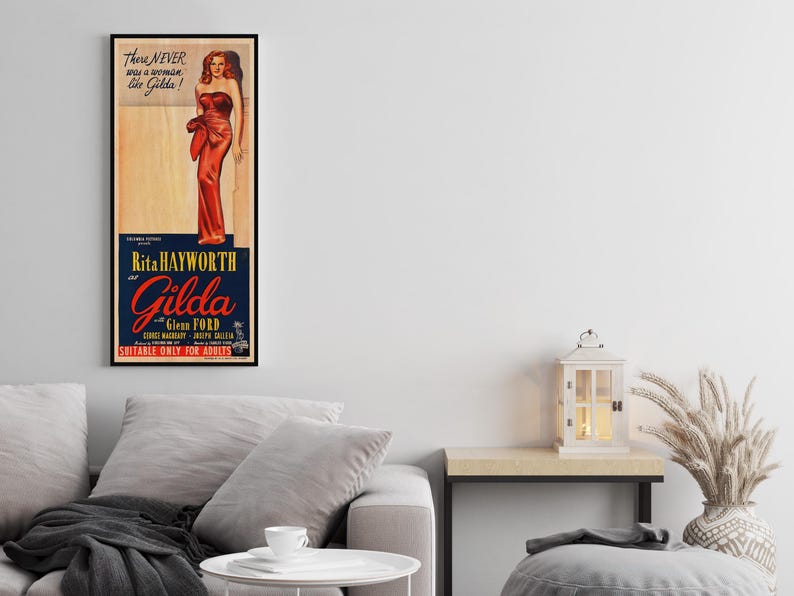 a framed vintage poster of a woman in a red dress, hanging on a wall above a gray couch in a living room setting.