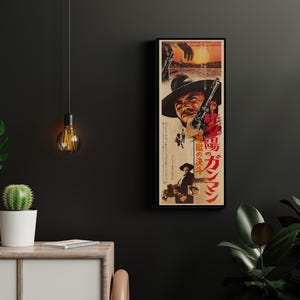a framed poster of a movie poster for "The Dark Knight" hanging on a wall, with a cactus plant and a hanging light fixture in the foreground.