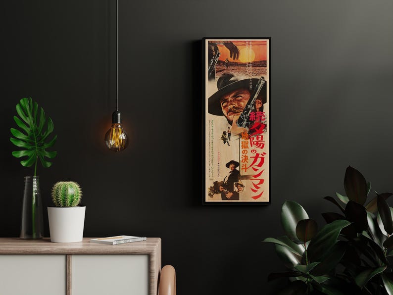 a framed poster of a movie poster for "The Dark Knight" hanging on a wall, with a cactus plant and a hanging light fixture in the foreground.