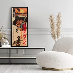 a poster of a man with a cowboy hat, a vase of dried flowers, and a white armchair in a living room setting.