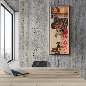 a wooden table with a laptop on it, situated in a room with a large window overlooking a cityscape. A framed poster of a man with a gun is hanging on the wall above the table.