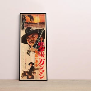 The image is a framed poster featuring a man with a gun, likely from a movie or film. The poster has a lot of text in Japanese, which is not transcribed here as it would result in redundancy and vague wording.