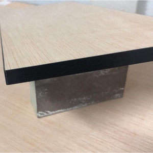 Puede incluir: Una mesa de madera clara con un borde negro, apoyada sobre un bloque de hormig&oacute;n gris.
