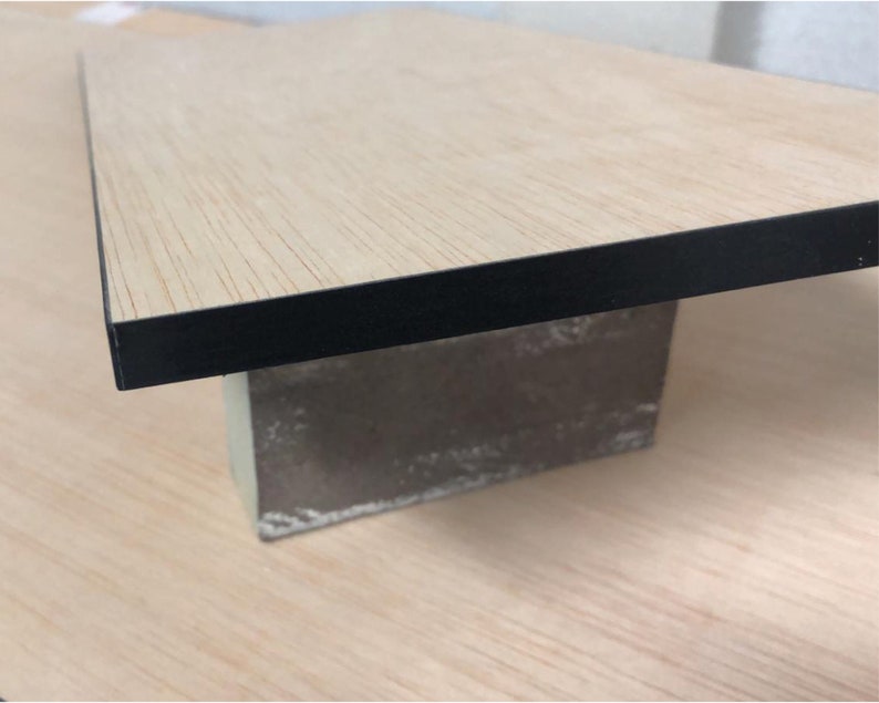Puede incluir: Una mesa de madera clara con un borde negro, apoyada sobre un bloque de hormig&oacute;n gris.