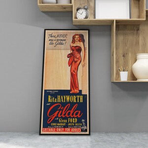 A framed vintage poster of Rita Hayworth in a red dress, standing on a wall next to a wooden shelf with a white vase and a clock.