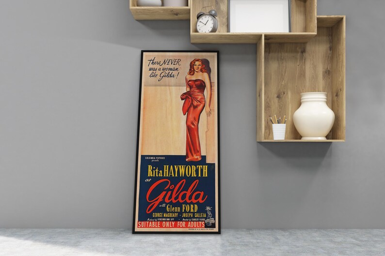 A framed vintage poster of Rita Hayworth in a red dress, standing on a wall next to a wooden shelf with a white vase and a clock.