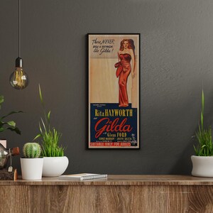 a framed vintage advertisement poster of a woman in a red dress, hanging on a wall above a wooden shelf with potted plants and other decorative items.