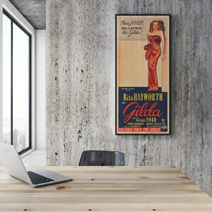 a wooden desk with a laptop on it, and a framed poster of a woman in a red dress hanging on the wall above the desk.