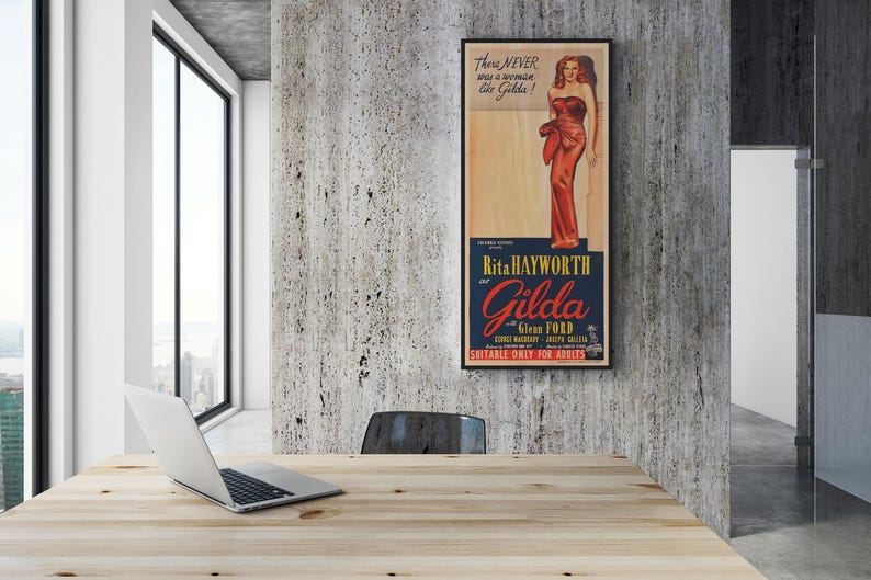 a wooden desk with a laptop on it, and a framed poster of a woman in a red dress hanging on the wall above the desk.