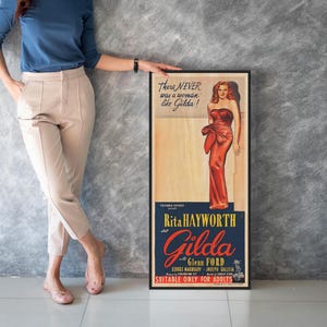 A woman is standing next to a framed poster featuring an illustration of a woman in a red dress.