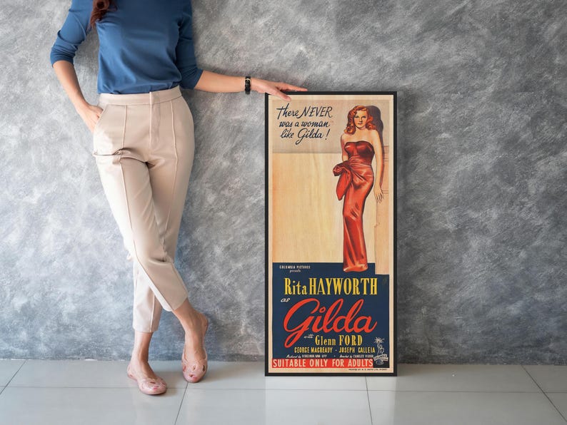 A woman is standing next to a framed poster featuring an illustration of a woman in a red dress.