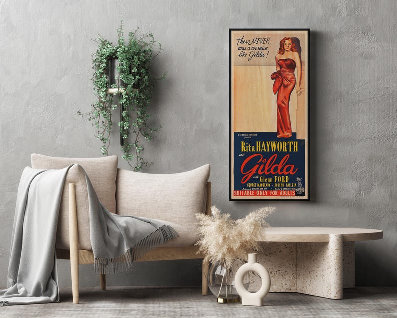 a living room setting with a sofa, a coffee table, and a potted plant. There is a framed poster of a woman in a red dress hanging on the wall, and a vase of flowers is placed on the coffee table.