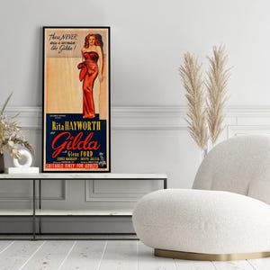 a framed vintage advertisement poster of Rita Hayworth and Gilda Gillett, with a white armchair and a potted plant in the foreground.
