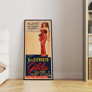 a framed poster of Marilyn Monroe in a red dress, standing in a room with a white couch and a bookshelf in the background.