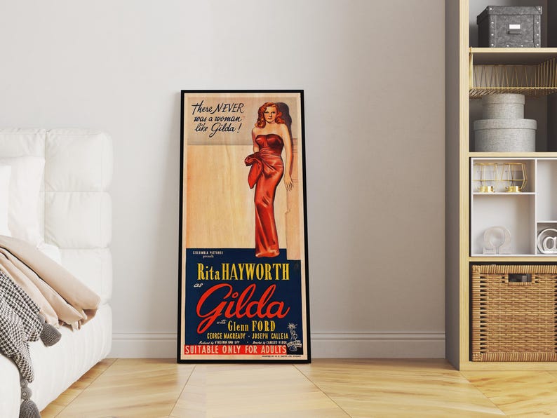 a framed poster of Marilyn Monroe in a red dress, standing in a room with a white couch and a bookshelf in the background.