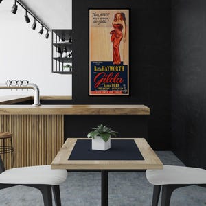 a modern interior design with a black and white color scheme. A wooden bar is situated in the background, and a table with two chairs is positioned in the foreground. A framed poster of a woman in a red dress is displayed on the wall, adding a decorative element to the space.