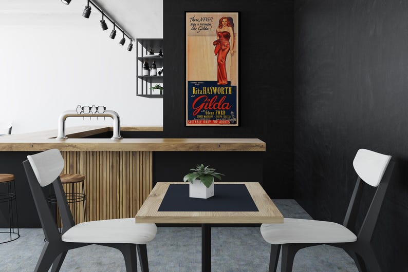 a modern interior design with a black and white color scheme. A wooden bar is situated in the background, and a table with two chairs is positioned in the foreground. A framed poster of a woman in a red dress is displayed on the wall, adding a decorative element to the space.