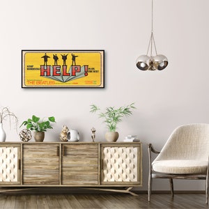 Puede incluir: Un p&oacute;ster de estilo vintage para la pel&iacute;cula de los Beatles "Help!" de 1965. El p&oacute;ster presenta un fondo amarillo con la palabra "HELP!" en letras rojas y los Beatles de pie sobre un libro. El texto "STOP!" y "IS ON THE WAY!" est&aacute; en letras negras.