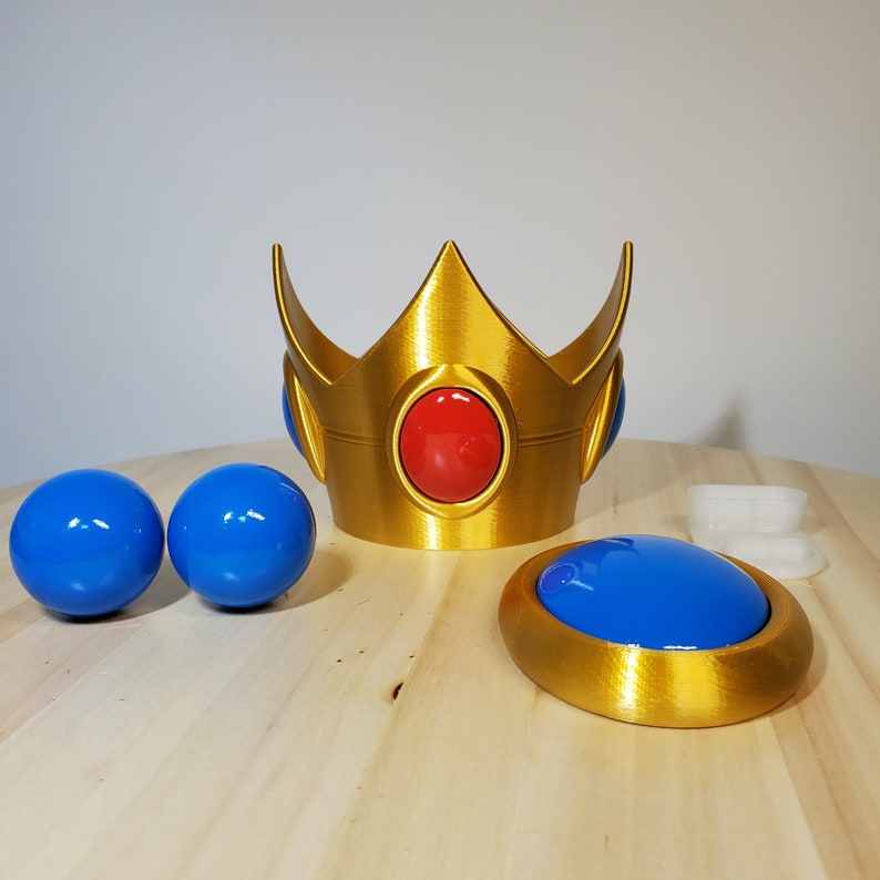 May include: A gold crown with a red jewel in the center and two blue jewels on the sides. There are two blue spheres and a gold button with a blue center.