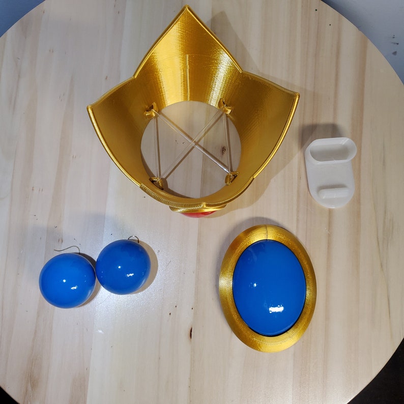 May include: A gold crown with a red jewel, two blue ball earrings, and a blue jewel with a gold rim.