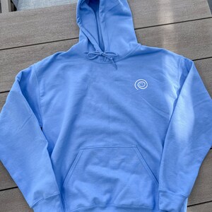 Peut inclure: Un sweat-shirt &agrave; capuche bleu clair avec un motif en spirale blanc sur le devant. Le sweat-shirt a une poche kangourou et une capuche &agrave; cordon.