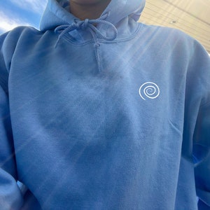 Peut inclure: Un sweat-shirt bleu clair avec un motif en spirale blanc sur le devant.