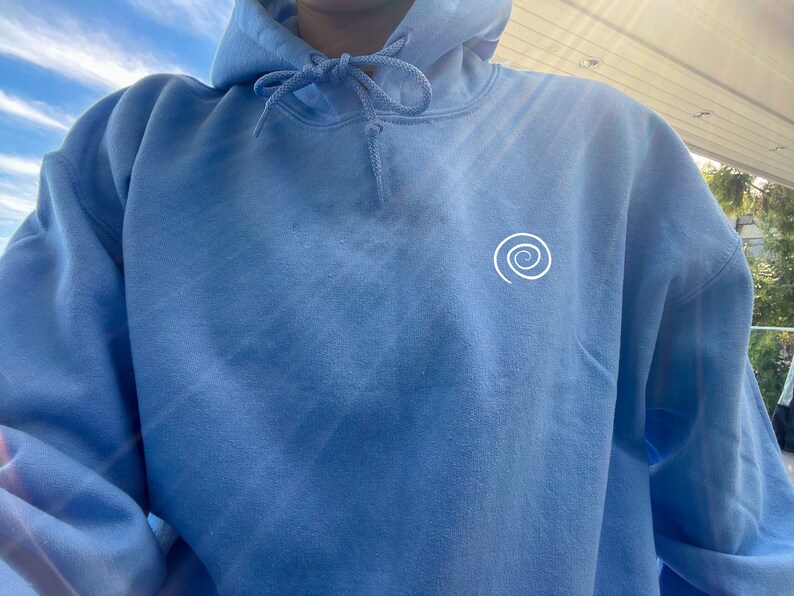Peut inclure: Un sweat-shirt bleu clair avec un motif en spirale blanc sur le devant.