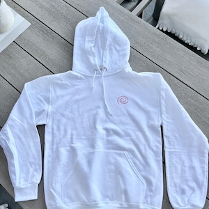 Peut inclure: Sweat-shirt &agrave; capuche blanc avec un petit motif en spirale rose sur le devant.