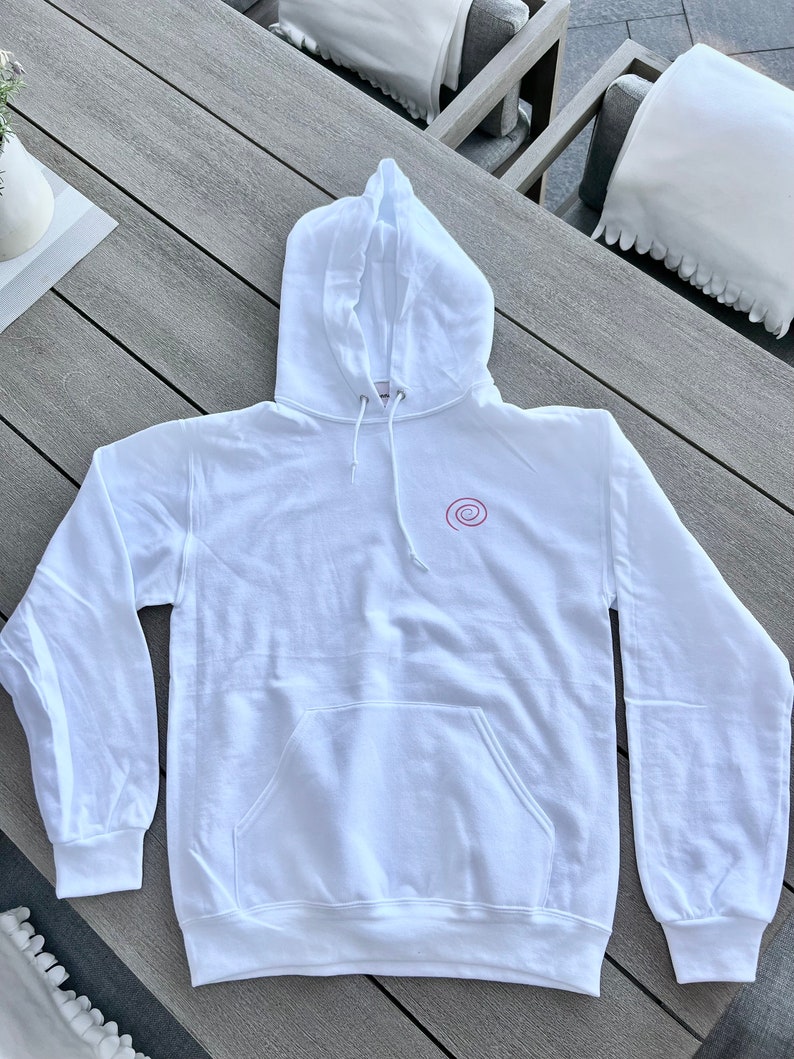 Peut inclure: Sweat-shirt &agrave; capuche blanc avec un petit motif en spirale rose sur le devant.