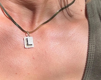 Colgante de collar con inicial L dorada, hecho a mano con cuentas tejidas.