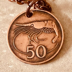 Puede incluir: Un collar con un colgante de cobre que presenta un diseño de camarón y el número "50" en la parte delantera. El colgante está unido a una cadena de cobre.