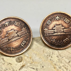 May include: Two copper Japanese coins with the text "日本国" and a depiction of a building. The coins are on a light brown surface.