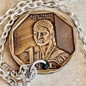 Könnte beinhalten: Eine silberne Kettenkette mit einem Anhänger aus einer bronzenen Münze. Die Münze zeigt ein Porträt von María Parado de Bellido, den Text "BICENTENARIO 1821-2021" und die Zahl "1".