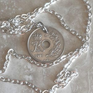 May include: A silver necklace with a coin pendant. The coin, dated 1971, features a crown and floral details. The chain is a simple link design. This necklace offers a classic, elegant style. The chain is suitable for everyday wear.
