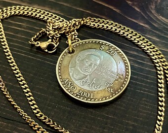 Könnte beinhalten: Eine goldfarbene Panzerkette mit einem runden Anhänger aus einer 20-Peso-Münze aus dem Jahr 2001. Die Münze zeigt ein Porträt, den Text $20, AÑO 2001, Octavio Paz und die Inschrift Todo es presencia, todos los siglos son este Presente.