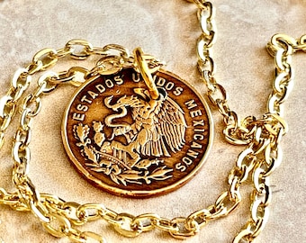 Könnte beinhalten: Eine goldfarbene Halskette mit einem runden Anhänger aus einer mexikanischen Münze. Die Münze zeigt einen Adler auf einem Kaktus mit einer Schlange im Schnabel, umgeben vom Text ESTADOS UNIDOS MEXICANOS. Der Anhänger hängt an einer Goldkette.