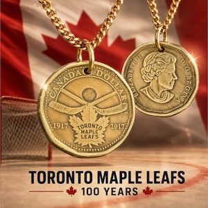 May include: Two gold-toned coin pendants on chains. One coin features crossed hockey sticks, a maple leaf, and the text "CANADA DOLLAR 1917 TORONTO MAPLE LEAFS 2017". The other coin shows a profile of Queen Elizabeth II with "ELIZABETH II D G REGINA".