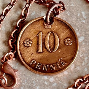 May include: A copper necklace with a 10 Pennia coin pendant. The coin is copper and has a floral design around the edge. The necklace is made of a copper chain.