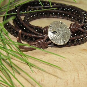 May include: A brown leather wrap bracelet with dark brown beads and a silver sand dollar charm.