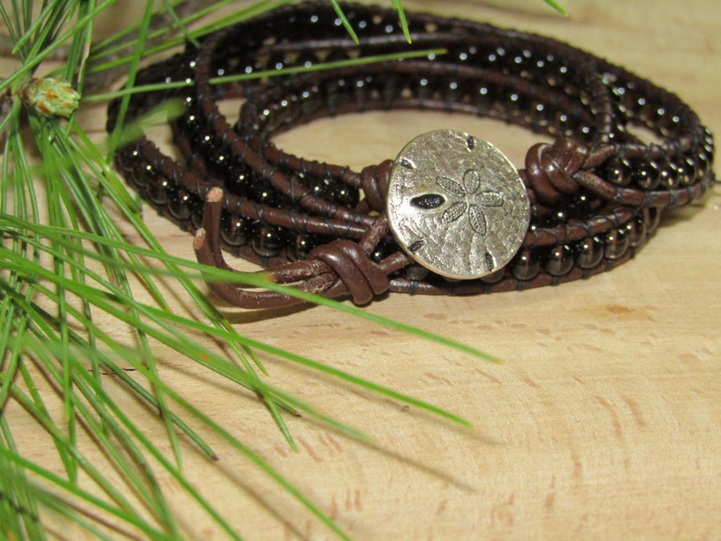 May include: A brown leather wrap bracelet with dark brown beads and a silver sand dollar charm.