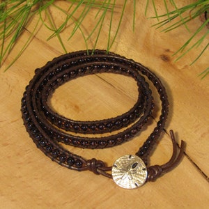 May include: A brown leather wrap bracelet with dark brown beads and a silver sand dollar charm.