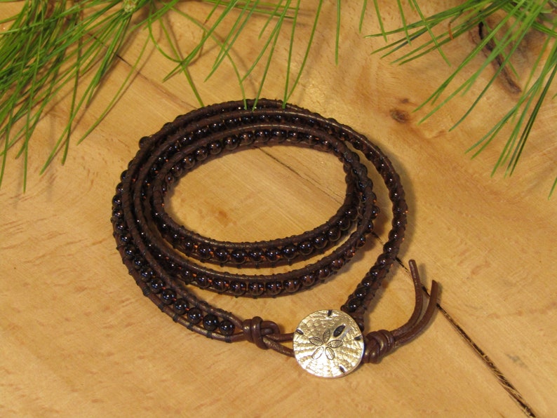 May include: A brown leather wrap bracelet with dark brown beads and a silver sand dollar charm.