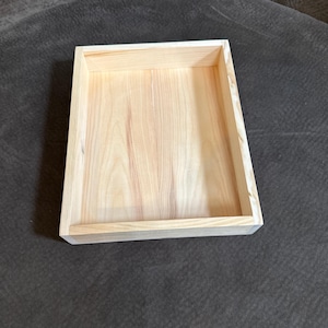 Op de afbeelding: Een rechthoekige houten dienblad met een glad, onafgewerkt oppervlak. Het dienblad is gemaakt van licht hout met een natuurlijke houtnerf.
