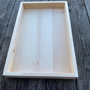 Könnte beinhalten: Ein schlichtes rechteckiges Holztablett. Das Tablett ist aus hellem Holz und hat eine glatte Oberfläche.