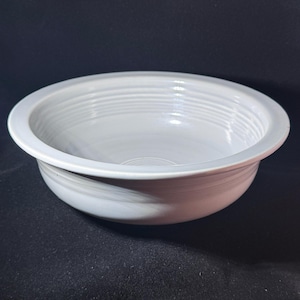 May include: A round, white ceramic bowl featuring a wide, flat rim and a series of concentric circular ridges along the interior wall. The bowl has a smooth, glossy finish and a deep, open basin, showcasing a clean, uniform white color throughout.